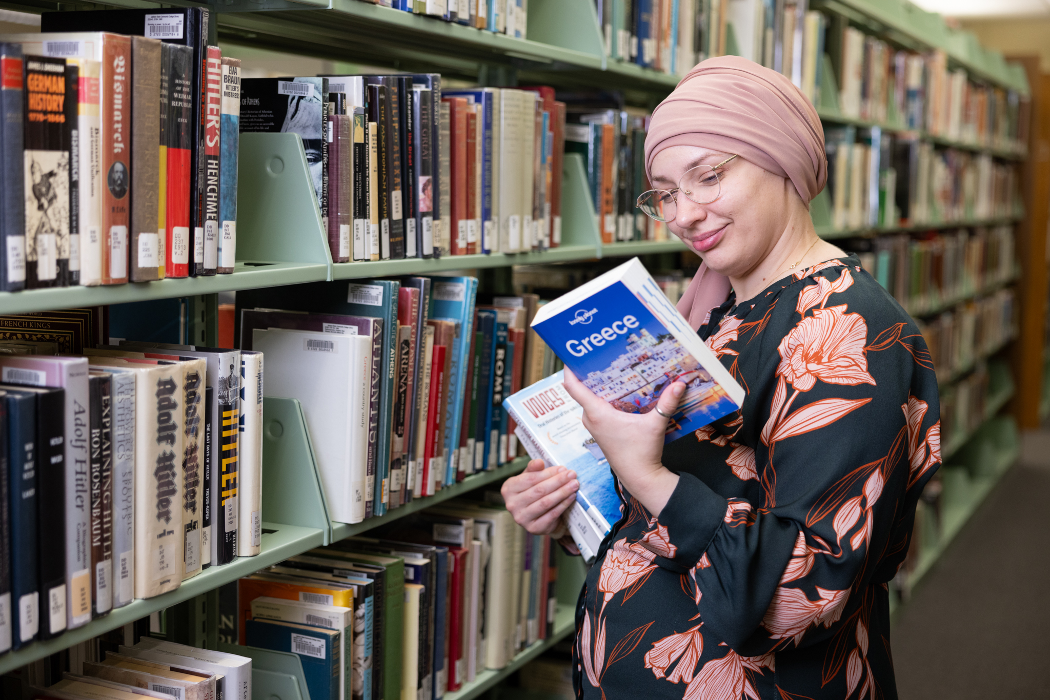 Student in Library choosing a book to read off of the shelf.
