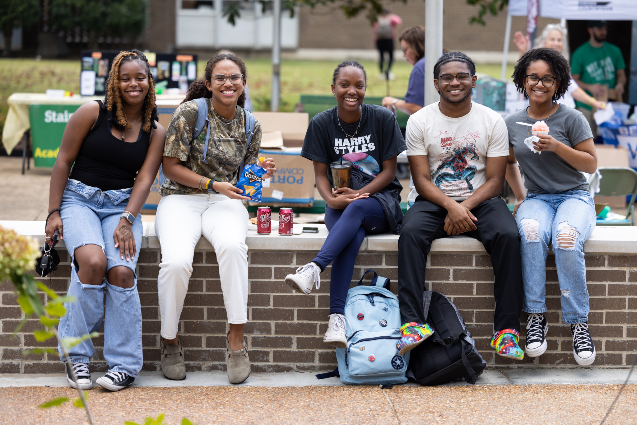 Students sitting on wall on campus eating food at an event and smiling.