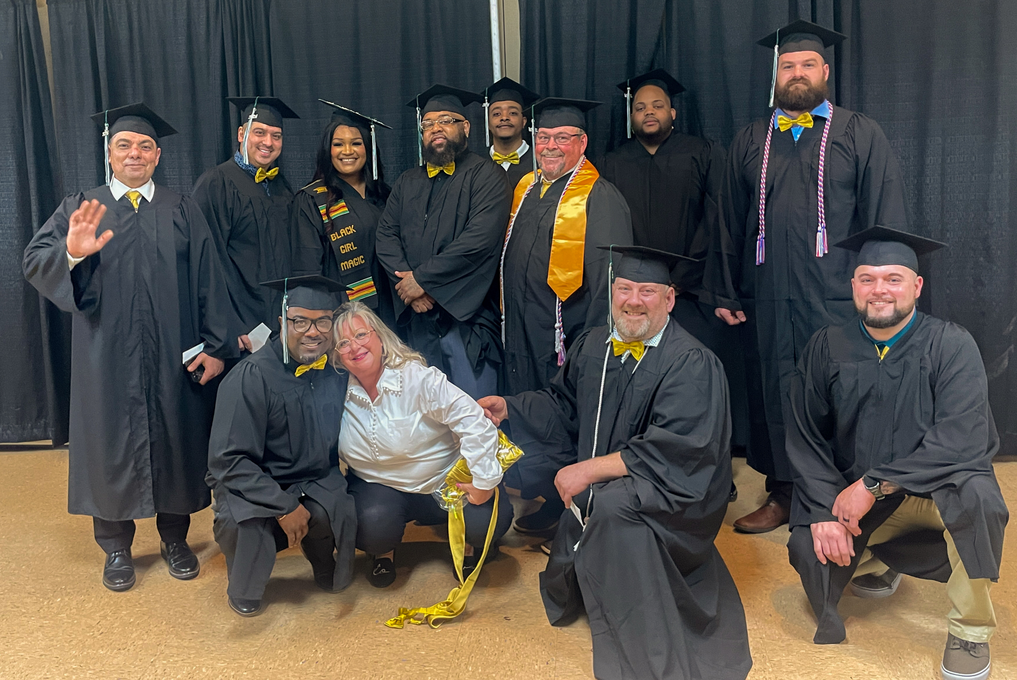 A group of ENST Evening Cohort graduates pose for a photo while wearing graduation gowns.