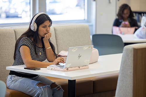A student wears headphones while working on a laptop in the study space of the newly renovated JSCC Learning Commons.